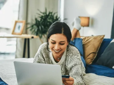 A woman in bed shopping online with a credit card.