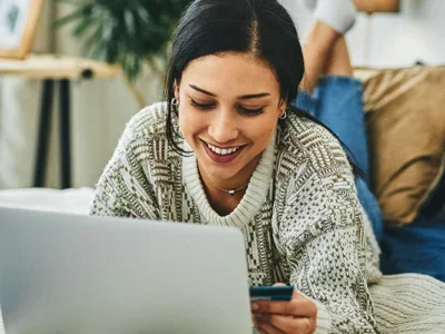 A woman in bed shopping online with a credit card.