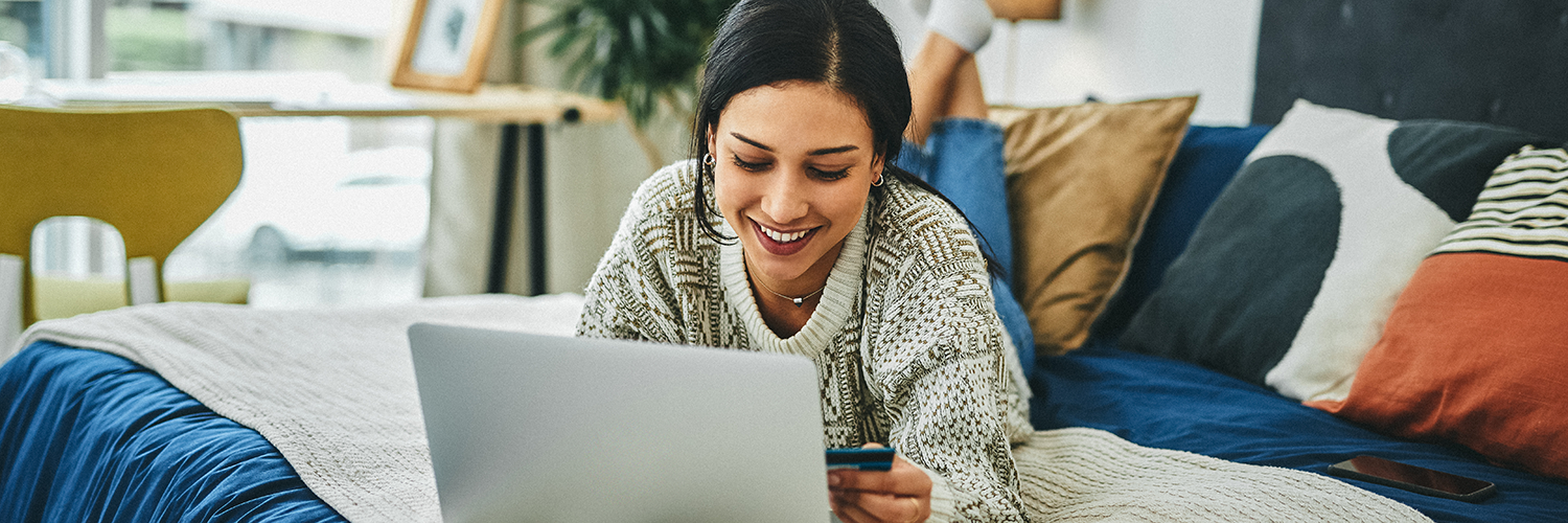 A woman in bed shopping online with a credit card.