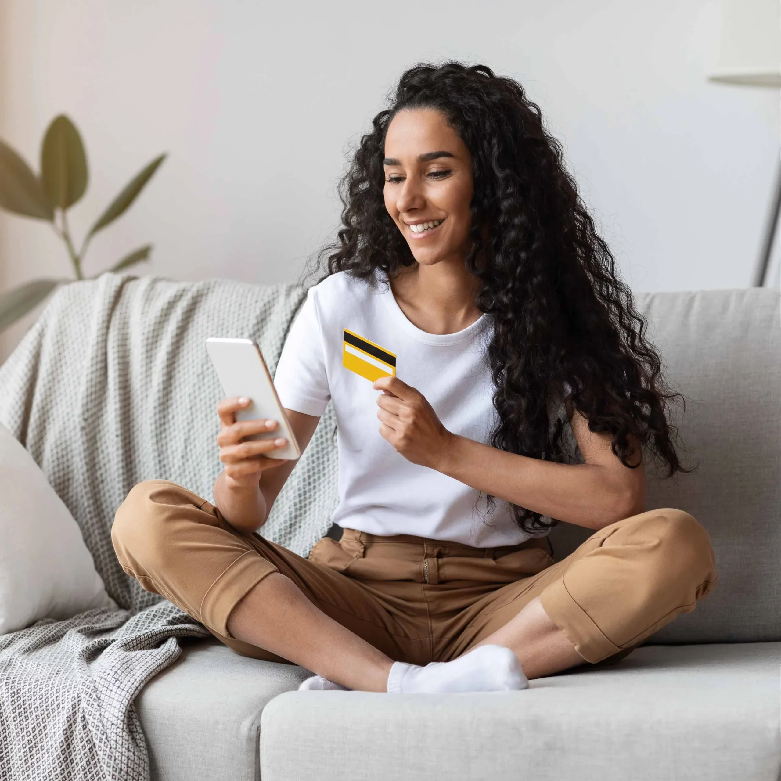 A woman on her couch making a personal loan payment with her credit card.