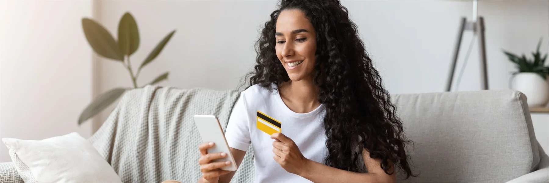 A woman on her couch making a personal loan payment with her credit card.